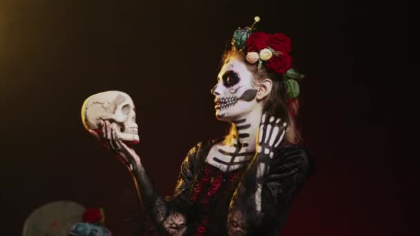 La Cavalera catrina puhuu pääkallolle studiossa, käyttäytyy pelottavasti ja kauhuissaan juhliakseen meksikolaista halloweenperinnettä. Santa Muerte pukeutunut kauhu pelottava puku kehon taidetta. Kämmentietokone. - Materiaali, video