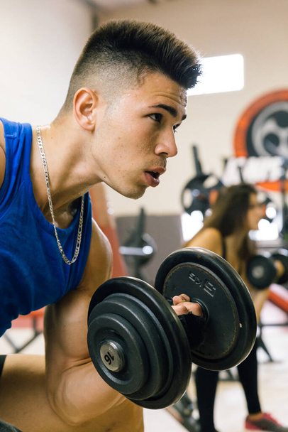 Young bodybuilder working out lifting dumbbells at the gym. - 写真・画像
