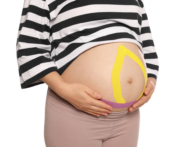 Pregnant woman with kinesio tapes on her belly against white background, closeup - 写真・画像
