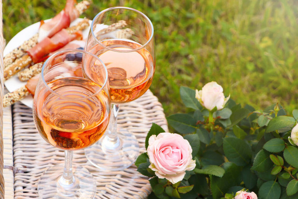 Flowers near glasses of delicious rose wine and food on picnic basket outdoors, closeup - Fotografie, Obrázek