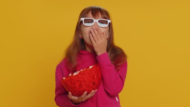 Podekscytowana młoda uczennica w okularach 3D jedząc popcorn, oglądając ciekawe seriale telewizyjne, gra sportowa, film, online social media treści filmowe. Nastolatka dziecko dziecko na studio żółty tle - Materiał filmowy, wideo