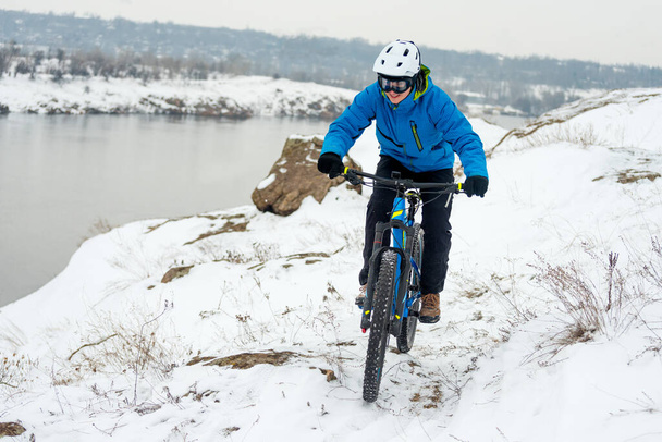 Cyclist in blue resting with mountain bike on rocky winter hill. Extreme sport and enduro biking concept. - Foto, afbeelding