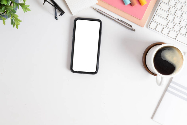 Top view smart phone with blank screen, coffee cup and stationery on white table. - 写真・画像