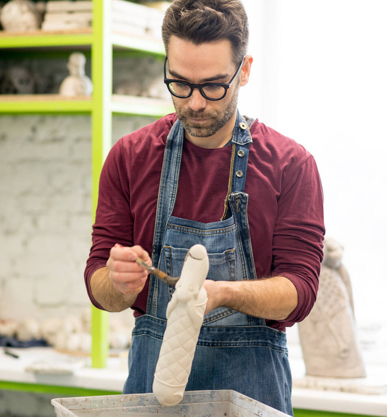 Portrait of ceramist dressed in an apron working on clay sculpture in bright ceramic workshop. - Photo, Image