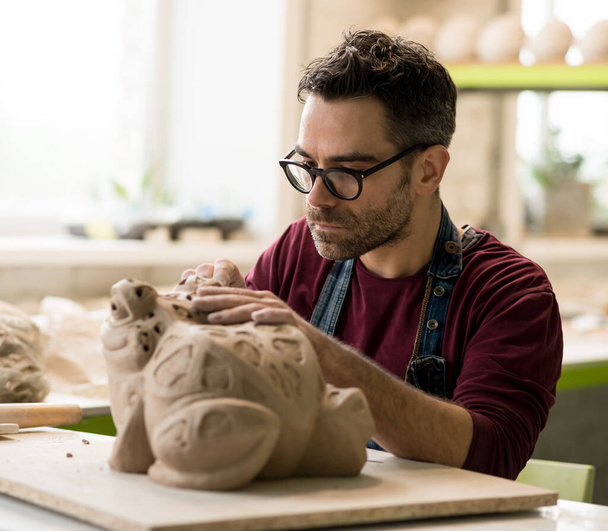 Portrait of ceramist dressed in an apron working on clay sculpture in bright ceramic workshop. - Photo, Image