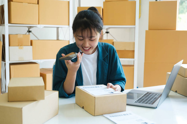 Young female small business enrtrepreneur, online store owner working on laptop with boxes on desk at warehouse talking with customer on the phone receiving, comfirming order. Online selling, e - Φωτογραφία, εικόνα