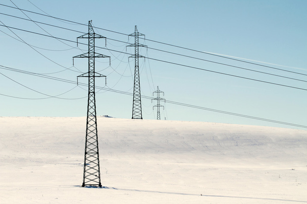 Υψηλής τάσης ηλεκτρικής ενέργειας ισχύος πυλώνα στο χιονισμένο πεδίο - Φωτογραφία, εικόνα