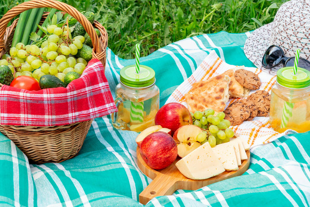 Picnic on the grass on a summer day - basket, grapes, cheese, bread, apples - a concept of summer outdoor recreation - 写真・画像