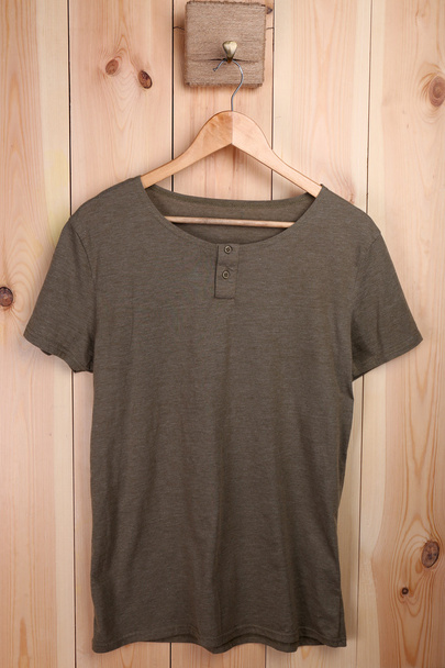 Male t-shirt on hanger on wooden wall background - Foto, afbeelding