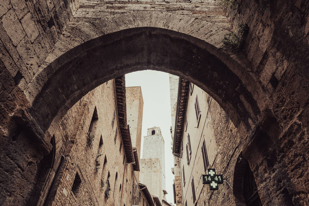 Vista de un arco de piedra en un callejón de una ciudad medieval. San Gimignano en la provincia de Siena, Toscana, centro-norte de Italia. - Foto, Imagen