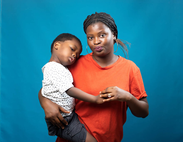 Šťastná africká matka, teta nebo poručník pečující o malého chlapce, když ho nosí v rukou a také se dívá do kamery - Fotografie, Obrázek