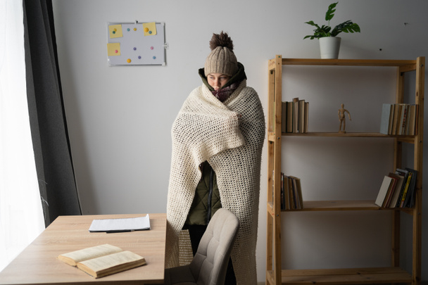 Angry girl student warmly dressed in a cold house suffering from cold at home, no heating and power concept - 写真・画像