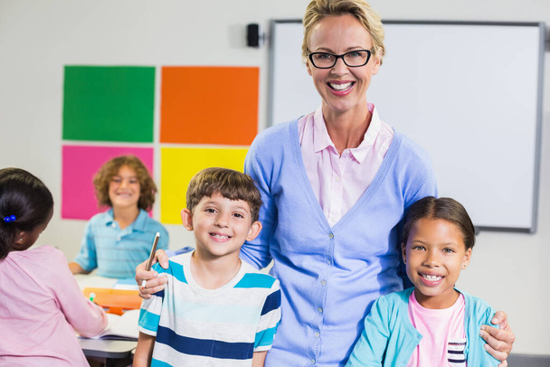 Πορτρέτο του χαμογελαστού δασκάλου και των παιδιών που στέκονται μαζί με τα χέρια - Φωτογραφία, εικόνα