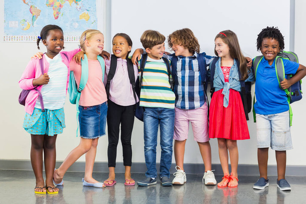 Lächelnde Kinder stehen mit dem Arm im Klassenzimmer herum - Foto, Bild