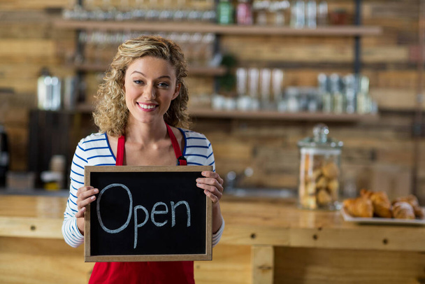 Smiling waitress standing with open signboard in cafe - Photo, Image