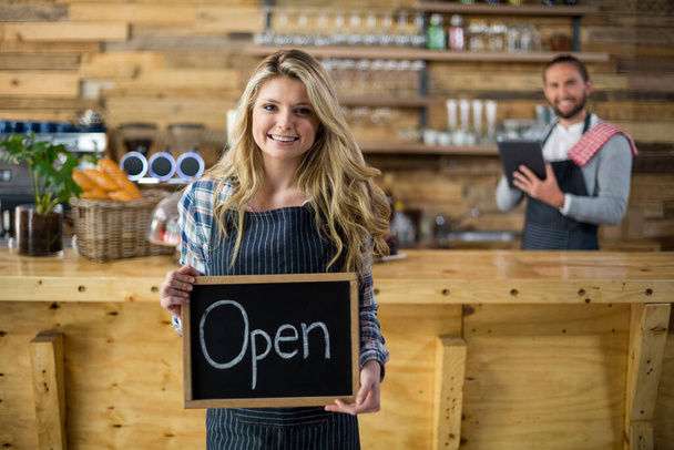 Lächelnde Kellnerin zeigt Schiefer mit offenem Schild im Café - Foto, Bild