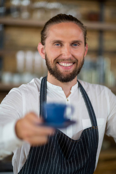 Muotokuva hymyilevä tarjoilija tarjoaa kupin kahvia
  - Valokuva, kuva