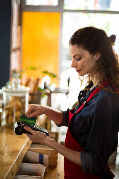 Kelnerka przesuwa kartę kredytową przez czytnik kart kredytowych w kasie - Zdjęcie, obraz