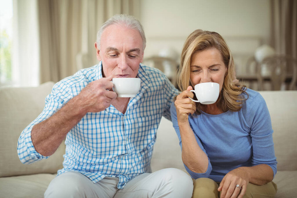 "Lächelndes Seniorenpaar bei einer Tasse Kaffee im Wohnzimmer" - Foto, Bild