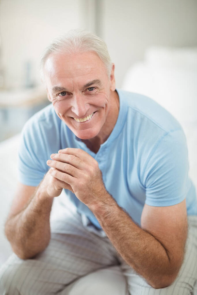 Πορτρέτο του χαμογελαστού άνδρα που κάθεται στο κρεβάτι  - Φωτογραφία, εικόνα