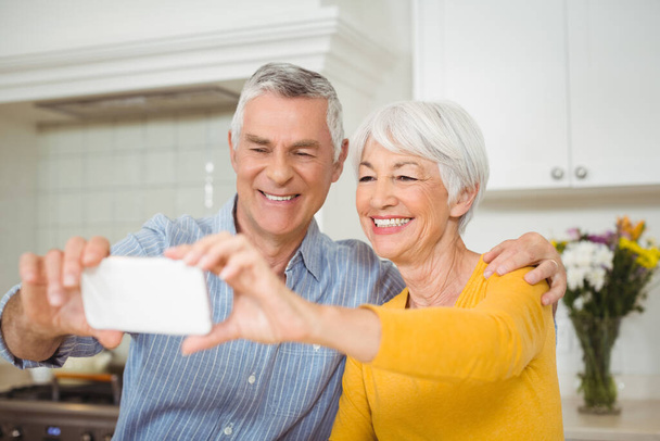 "Couple de personnes âgées prenant selfie à partir d'un téléphone mobile dans la cuisine
" - Photo, image