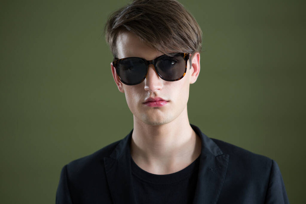 Androgynous man in sunglasses posing against green background - Photo, Image