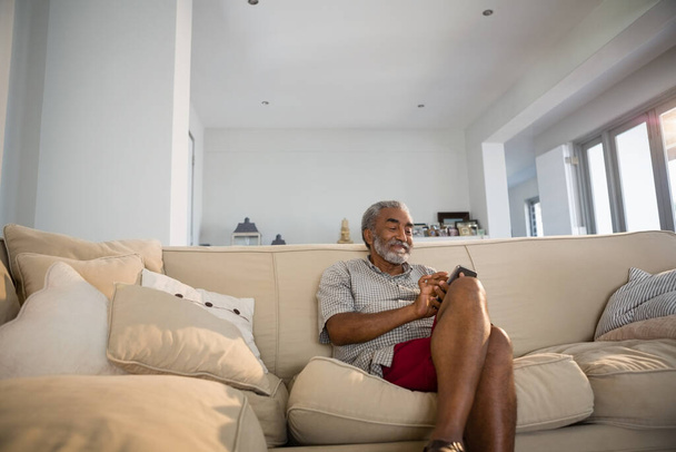 Hombre mayor usando teléfono móvil en la sala de estar - Foto, imagen