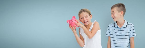 Happy boy and girl holding a piggy bank against blue background - Foto, Bild