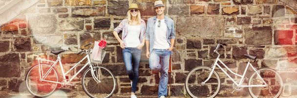 Молодая пара, стоящая у кирпичной стены с велосипедами - Фото, изображение