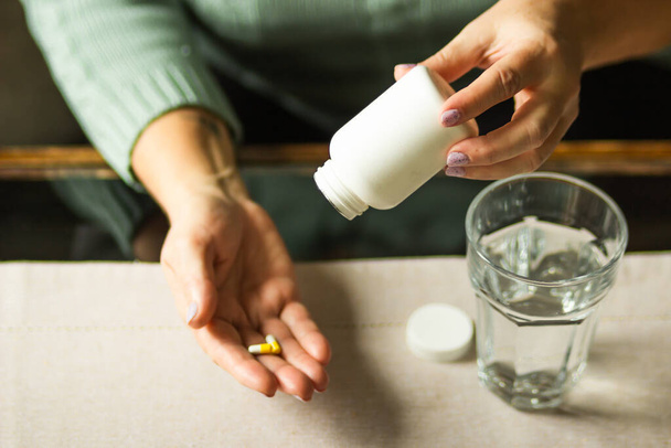 Elderly woman holding white plastic bottle with pills and two capsules in her hand, ready to take supplement pills with glass of water. Sick senior woman taking medication. Health care concept. - Photo, Image