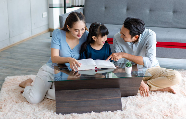 Millennial asiática feliz familia padre y madre sentado en acogedor suelo de alfombra sonriendo ayudar a enseñar niña pequeña hija leyendo estudiar aprendizaje con gran libro de texto en la sala de estar en casa. - Foto, imagen