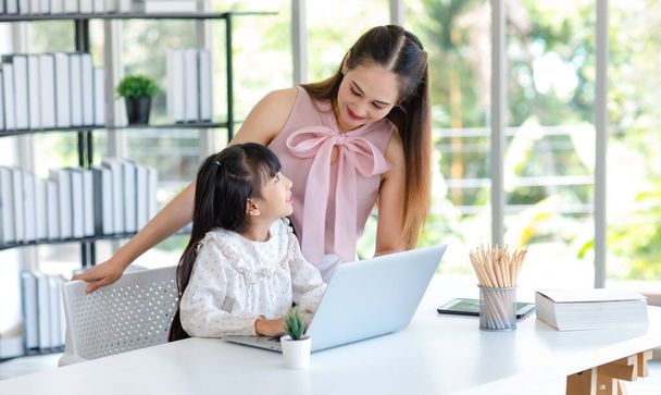 Millennial asiática feliz familia madre sonriendo ayudar a apoyar la enseñanza niña niña hija estudiando aprendizaje haciendo tarea de la escuela en línea a través de ordenador portátil portátil en la sala de estar en casa. - Foto, imagen