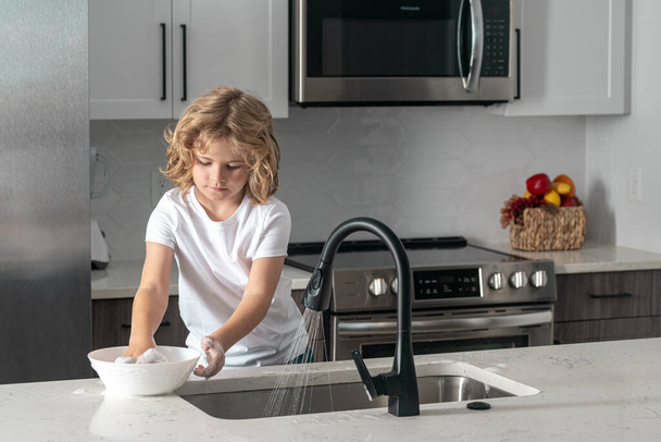 Child cleaning dishes with sponge. Cleaning supplies. Help clean-up. Housekeeping duties. Kid wash dishes. Child help in washing dishes at kitchen - Foto, imagen