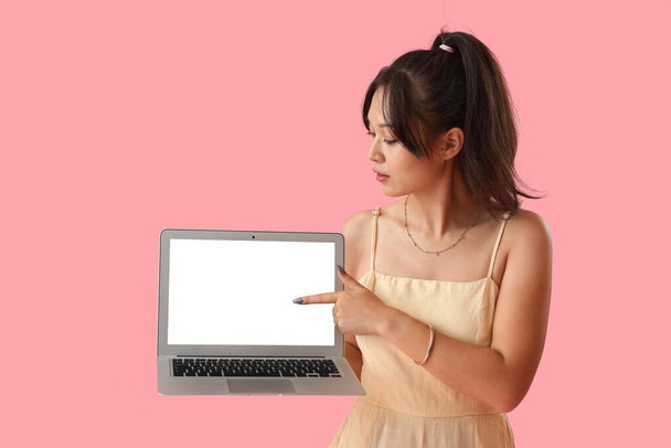 Jovem mulher asiática apontando para laptop no fundo rosa - Foto, Imagem