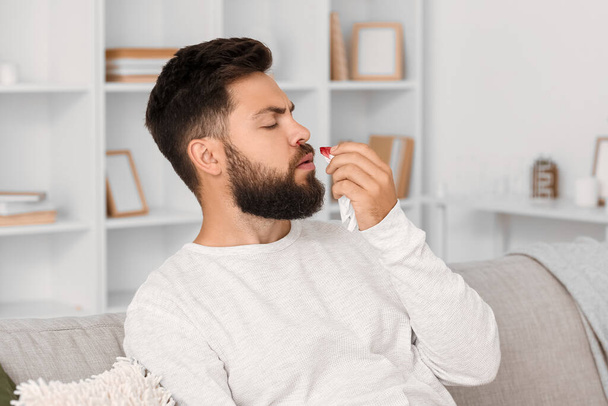 Young bearded man with nosebleed and tissue at home - Foto, afbeelding