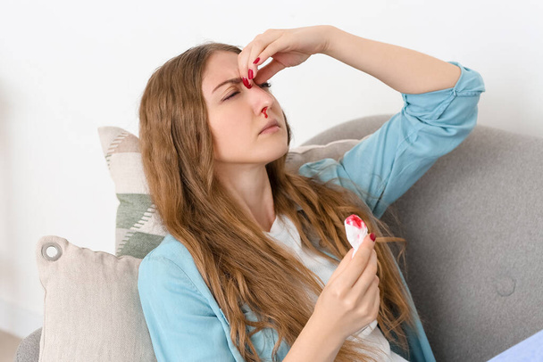 Mujer joven con hemorragia nasal y tejido en casa - Foto, Imagen