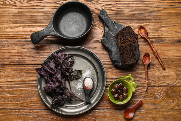 Küchenutensilien mit Brotscheiben, Oliven, Meersalz und Basilikum auf Holzgrund - Foto, Bild