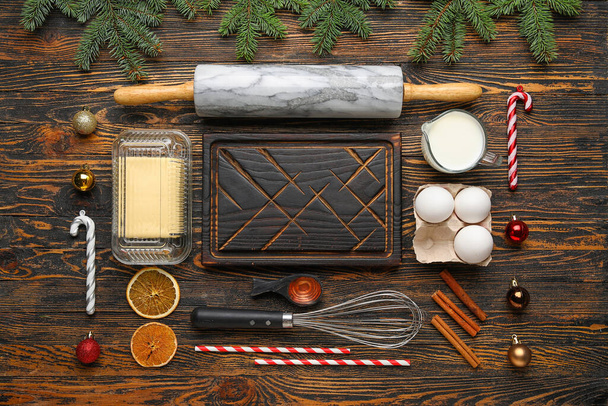 Řezací deska, ingredience a nádobí pro přípravu vánočních sušenek na dřevěném pozadí - Fotografie, Obrázek