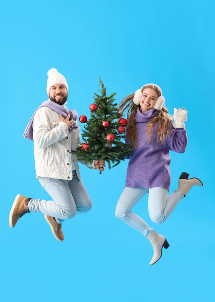 jong paar met kerstboom springen op blauwe achtergrond - Foto, afbeelding