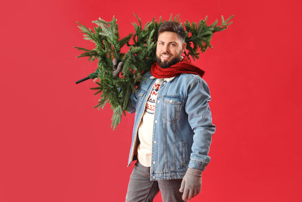Όμορφος άντρας με χριστουγεννιάτικο δέντρο σε κόκκινο φόντο - Φωτογραφία, εικόνα