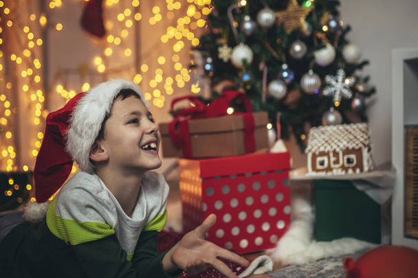Onnellinen poika makaa edessä lattialla joulukuusi ympäröi lahjoja. - Valokuva, kuva