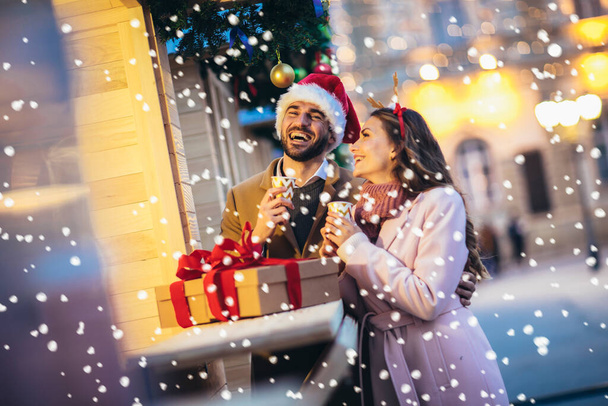 Молодая романтическая пара, держащая подарочную коробку, веселится на улице зимой перед Рождеством. - Фото, изображение