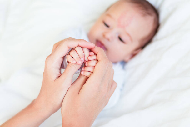 Η μητέρα κρατάει τα χέρια του νεογέννητου μωρού. Μικρά δάχτυλα στο χέρι της γυναίκας. Ζεστό πρωινό στο σπίτι - Φωτογραφία, εικόνα