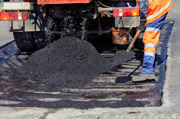 Trabajador de la carretera distribuye un pedazo de asfalto con una pala para el parche de la carretera - Foto, Imagen
