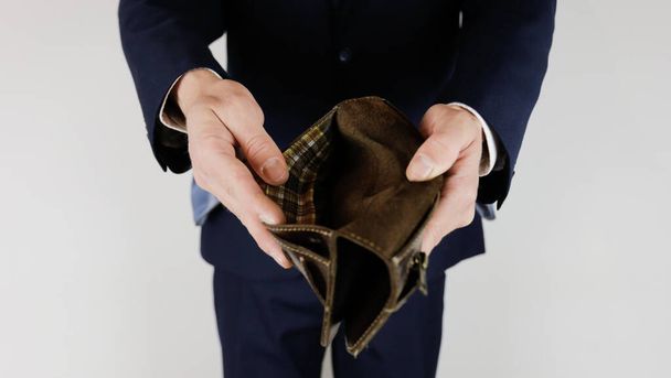 Een man in een zakenpak heeft een lege portefeuille in zijn handen.  - Foto, afbeelding