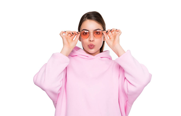 Portrait of fashion woman pouting lips adjusting pink glasses in casual hoodie isolated on white. - Fotoğraf, Görsel
