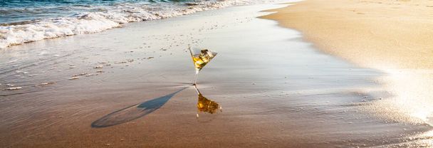bebida en vaso de martini lavado por agua de mar en la playa de arena - Foto, imagen