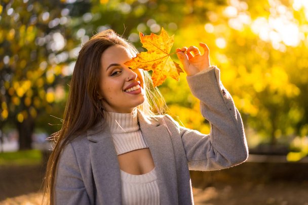A pretty woman enjoying autumn in a park at sunset, with a leaf on her face - Foto, Imagem
