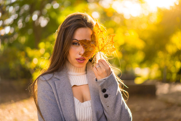 A pretty woman enjoying autumn in a park at sunset, with a leaf from the tree - Foto, Imagem
