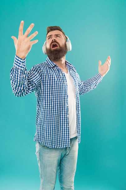 zingende bebaarde man in casual geruite shirt luisteren lied in heaphones op blauwe achtergrond, muziek. - Foto, afbeelding